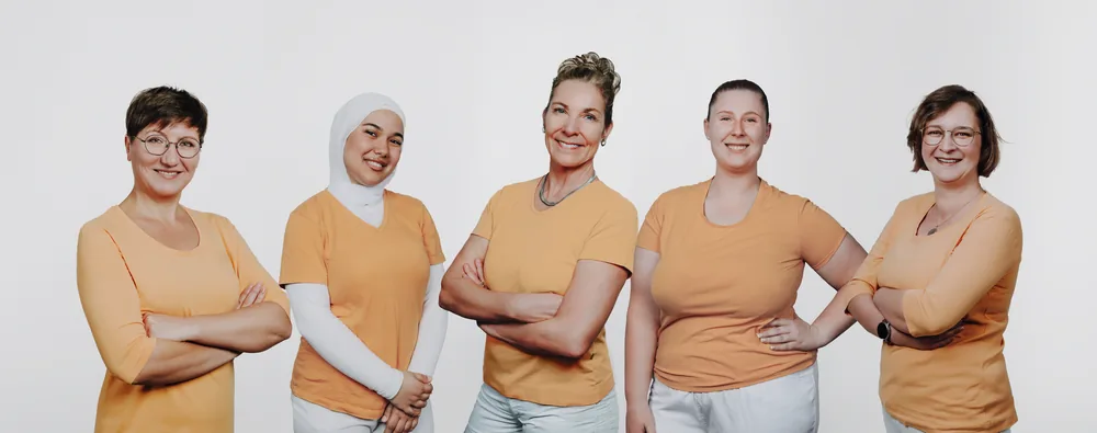 Das Team der Zahnarztpraxis Hansen in orangefarbener Praxiskleidung